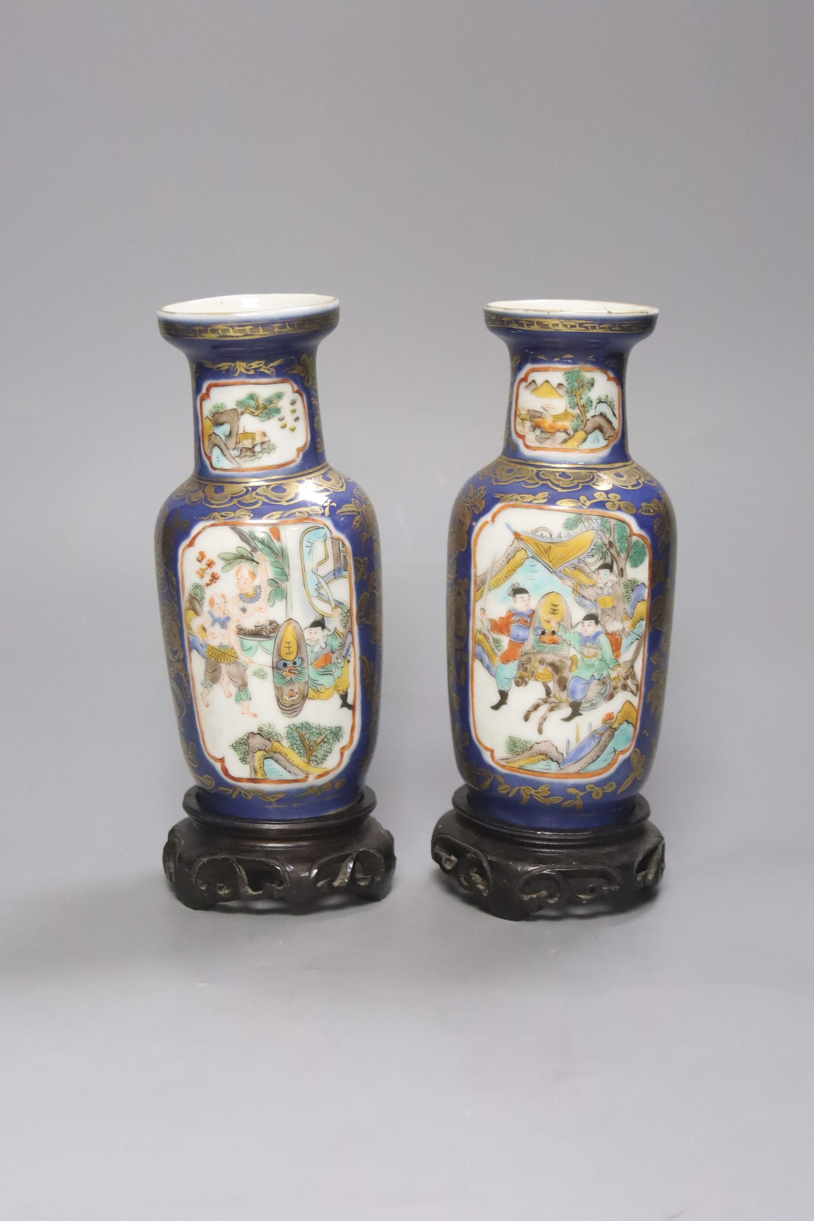 A pair of Chinese Kangxi style blue-ground vases, late 19th century decorated with panels of warriors and heightened in gilt, on carved hardwood stands, height 18cm excluding stand